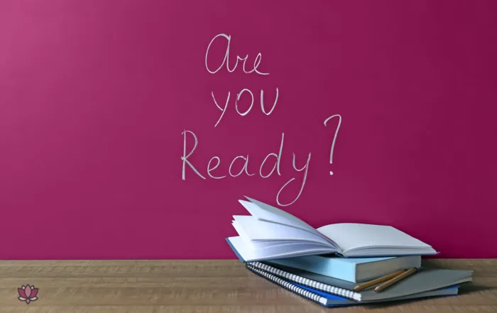 A desk with some work related items on it, with a sign on the wall saying "Are you ready?"