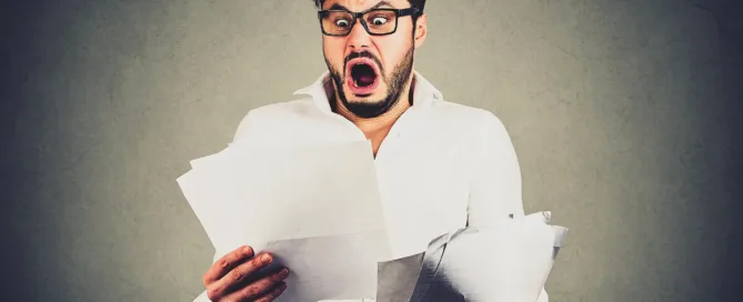 A man looks shocked as he looks at all the unpaid invoices he has in his hands